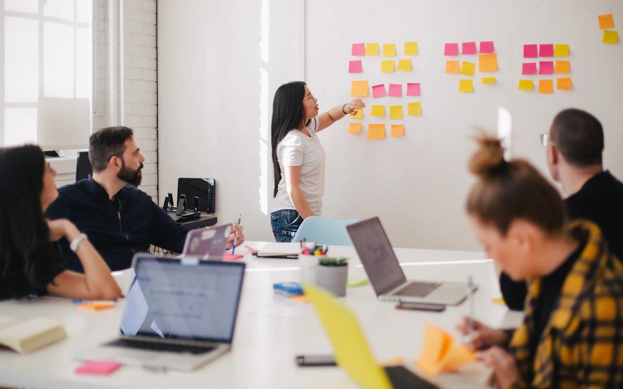 Someone at a wall of sticky notes talking a seated team through a process.