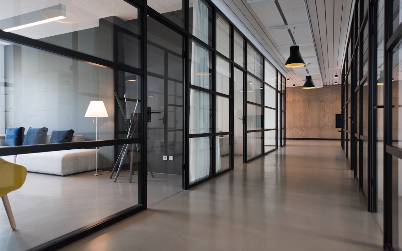 An empty office corridor lined with glass-walled meeting rooms.